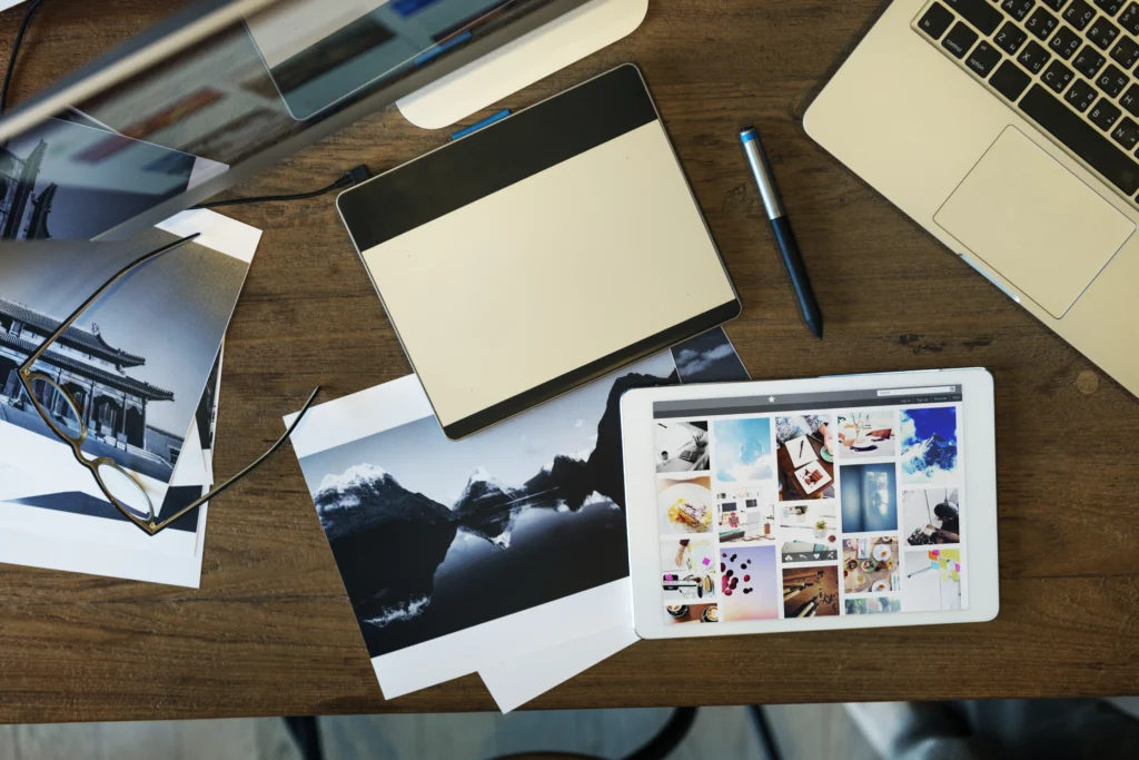 Overhead view of a GrowEasy digital marketing professional's desk with a laptop, design tablet, and printed photo examples.